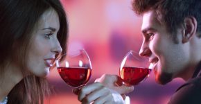 Young happy amorous couple with glasses of redwine on romantic date at restaurant