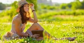 beautiful girl wearing hat with book sitting on grass and looking far away